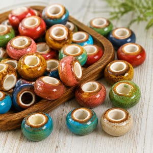 May include: A collection of round, ceramic beads with a glossy, crackled glaze finish in various colors including red, blue, green, and yellow. Each bead features a wide, white center hole and a smooth, rounded exterior surface.