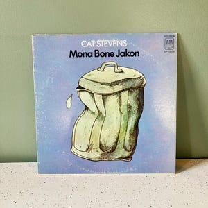 May include: Album cover for Cat Stevens' "Mona Bone Jakon" on a light blue background. The cover art features a watercolor illustration of a green trash can with a lid, appearing slightly crushed, with a white drip.