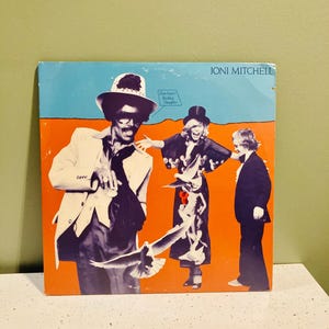 May include: Joni Mitchell album cover featuring a stylized illustration with figures and doves against a blue and orange background. The album title is displayed at the top right. The cover art has a vintage aesthetic.