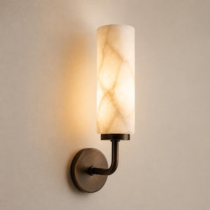 May include: A wall-mounted light fixture featuring a cylindrical, translucent white stone shade with natural veining. The shade is supported by a dark bronze-toned metal arm and a circular wall plate, emitting a warm, soft glow from within.