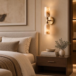 May include: A wall-mounted light fixture featuring two cylindrical, marbled, cream-colored glass shades stacked vertically. The shades are connected by a central brass-toned metal rod and attached to the wall with a circular brass-toned base.