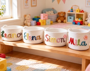 May include: Four round white rope baskets with integrated handles, each featuring a personalized name stitched in colorful yarn on the front. The names Leano, Elena, Simon, and Mila are displayed in cursive script, with small flower accents.