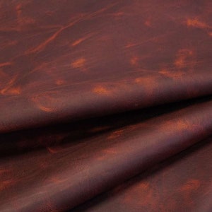 May include: Close-up of a piece of brown leather with a distressed, vintage look. The leather has a reddish-brown color with a subtle orange hue.