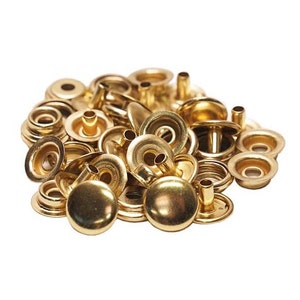Pode incluir: Um monte de bot&otilde;es de press&atilde;o de metal dourado. Os bot&otilde;es de press&atilde;o s&atilde;o feitos de duas partes, uma parte superior redonda e uma base plana com um poste.