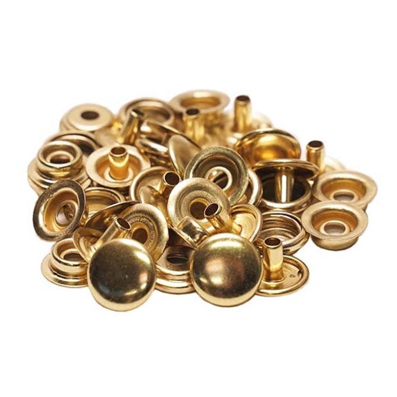 Pode incluir: Um monte de bot&otilde;es de press&atilde;o de metal dourado. Os bot&otilde;es de press&atilde;o s&atilde;o feitos de duas partes, uma parte superior redonda e uma base plana com um poste.