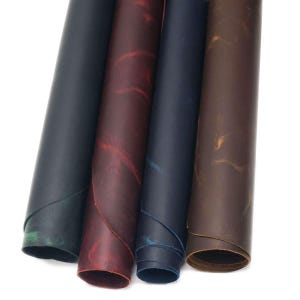 May include: Four rolls of leather material displayed side by side. The rolls are colored in deep black, a rich burgundy with red undertones, a dark navy blue, and a warm chocolate brown, each featuring a smooth, matte, and slightly distressed finish.