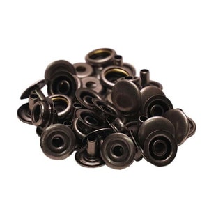 Pode incluir: Um monte de bot&otilde;es de press&atilde;o de metal preto, tamb&eacute;m conhecidos como poppers ou bot&otilde;es de press&atilde;o. Os bot&otilde;es de press&atilde;o est&atilde;o em diferentes est&aacute;gios de montagem, alguns t&ecirc;m a tampa superior presa e outros t&ecirc;m a base e o pino.