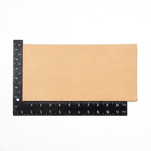 May include: A close-up of a light brown leather piece measured with a black ruler. The leather is 11 inches long and 6 inches wide.