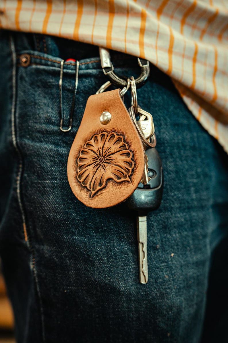 May include: A brown leather keychain with a tooled floral design. The keychain is attached to a pair of keys and a silver key ring.
