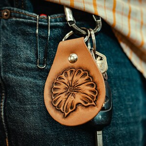 May include: A brown leather keychain with a tooled floral design. The keychain is attached to a silver key ring with keys.