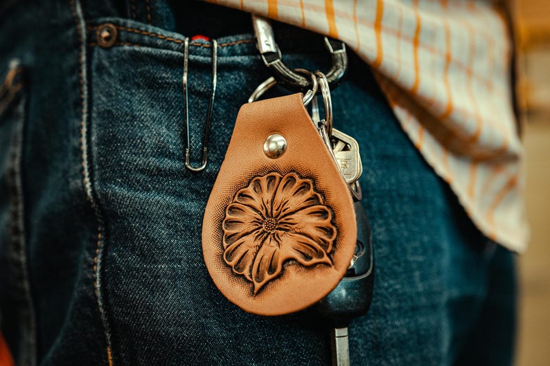 May include: A brown leather keychain with a tooled floral design. The keychain is attached to a silver key ring with keys.