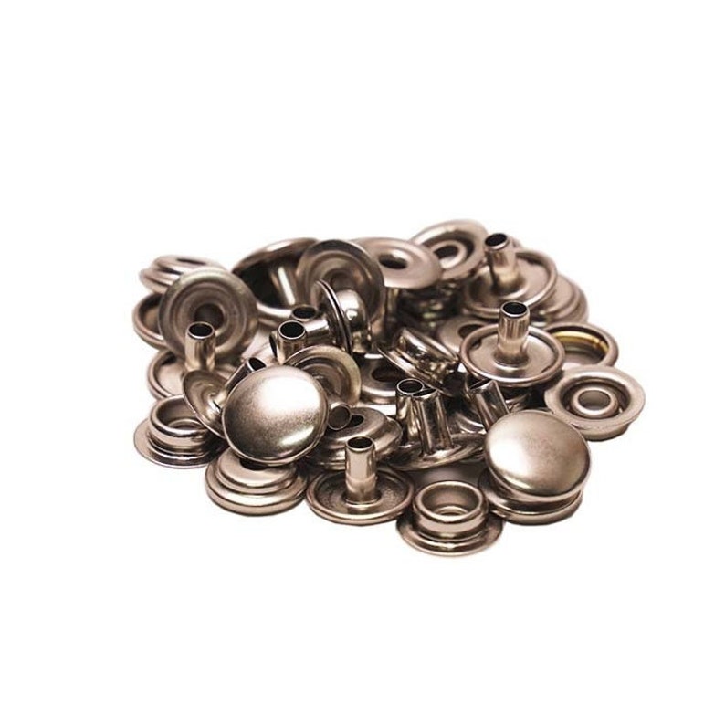 Pode incluir: Um monte de bot&otilde;es de press&atilde;o de metal prateado, tamb&eacute;m conhecidos como poppers, para unir tecidos. Estes s&atilde;o comumente usados para roupas, bolsas e outros trabalhos manuais.