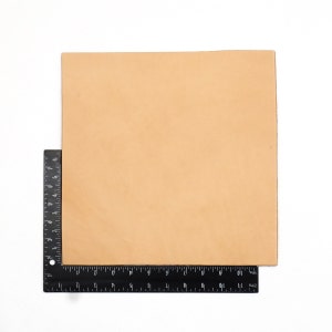 May include: A square, tan leather hide with a black ruler along the bottom and left side. The ruler shows measurements in inches. The leather has a smooth surface and is set against a white background.
