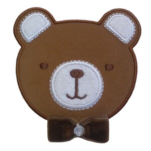 Könnte beinhalten: Braunes Filz-Bären-Applikationsmotiv mit weißen Filzohren, Nase und Mund. Der Bär trägt eine braune Samt-Schleife.