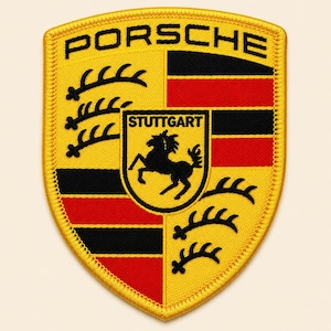May include: A shield-shaped embroidered patch featuring the Porsche logo in black text at the top. The design includes a central crest with a black horse and the word Stuttgart, surrounded by alternating yellow, black, and red sections with black antlers.