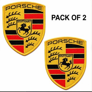 May include: A pack of two embroidered Porsche crest patches featuring the iconic shield design with black, red, and yellow colors. The patches display the word PORSCHE at the top and STUTTGART in a central shield with a black horse silhouette.