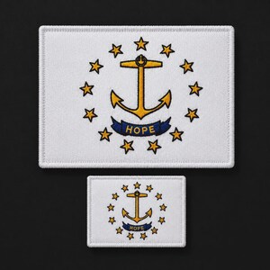 Puede incluir: Dos parches rectangulares bordados con el diseño de la bandera del estado de Rhode Island. Cada parche blanco muestra un ancla dorada en el centro, rodeada por trece estrellas doradas en círculo, con una cinta azul debajo que dice HOPE.