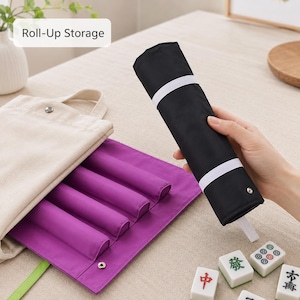 May include: A purple fabric roll-up storage mat with four cylindrical compartments, paired with a beige canvas tote bag and a black roll-up cover featuring white elastic bands. Several white mahjong tiles with green and red symbols are visible.