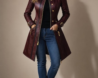 May include: A burgundy leather coat featuring a high collar, gold-tone buttons, and a front zipper closure. The coat has ribbed detailing on the shoulders and sleeves, adjustable buckled cuffs, and zippered pockets, worn over a black turtleneck.