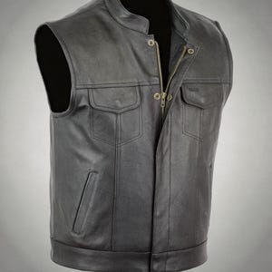 Könnte beinhalten: Eine schwarze Lederweste mit Stehkragen, Frontreißverschluss und zwei Brusttaschen mit Klappen. Das Kleidungsstück verfügt über zwei vertikale Seitentaschen sowie eine Druckknopfleiste, die den Reißverschluss verdeckt, mit glatter Oberfläche.
