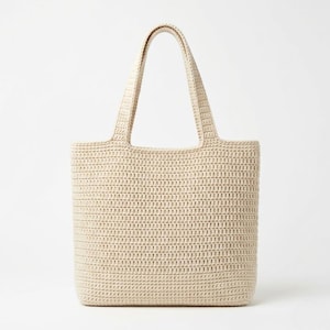 May include: A beige tote bag constructed from a dense, uniform crochet stitch pattern. The bag features a rectangular body with a flat base and two integrated shoulder straps that extend from the top edge, maintaining a consistent light tan color.