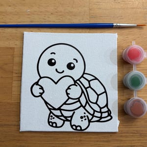 May include: A square white canvas featuring a black line art illustration of a smiling turtle holding a heart. A blue paintbrush with a silver ferrule is positioned above the canvas, and three small circular paint pots containing red, green, and brown paint are aligned vertically to the right.