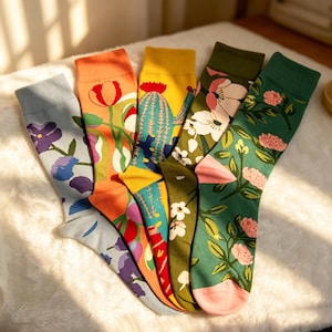 May include: A set of five crew socks featuring diverse botanical and desert patterns. The designs include purple flowers on light blue, red tulips on orange, a green cactus on yellow, white blossoms on olive green, and pink flowers on dark green.