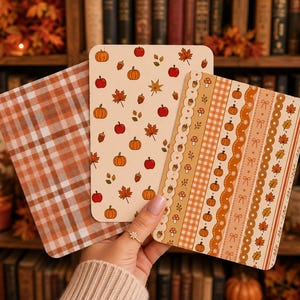 May include: Three rectangular cards with rounded corners featuring autumn-themed designs. One card has a brown and white gingham pattern, another displays a scattered print of pumpkins, apples, and leaves, and the third features vertical stripes.