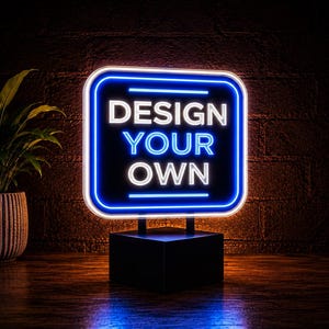 May include: A rectangular neon sign with rounded corners featuring the white and blue text "DESIGN YOUR OWN" illuminated against a dark background. The sign is mounted on a solid black rectangular base, creating a bright glowing display.