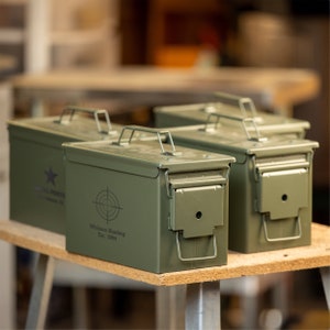 Peut inclure: Trois bo&icirc;tes &agrave; munitions en m&eacute;tal vert olive avec couvercles &agrave; charni&egrave;re et poign&eacute;es de transport. Les bo&icirc;tes ont une forme rectangulaire et sont &eacute;tiquet&eacute;es avec du texte blanc et un graphique de cible. Le texte indique "Whitson Hunting Est. 1994" et "HOUSTON, TX".