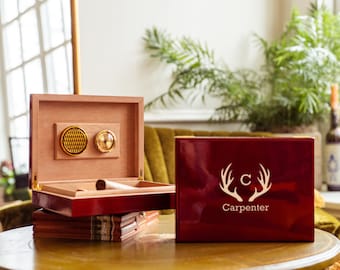 May include: A red wooden box with a gold-colored hinge and a gold-colored compass on the lid. The box has a white deer head design with the letter "C" and the word "Carpenter" on the front.