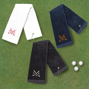 May include: Three golf towels with personalized embroidered initials and crossed golf clubs. The towels are white, navy blue, and black.