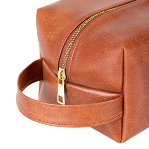 May include: A brown leather travel bag with a gold zipper and a brown leather handle.
