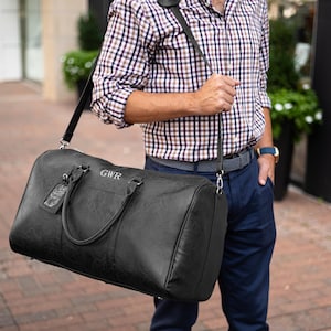 A man holding a black leather duffle bag over his shoulder