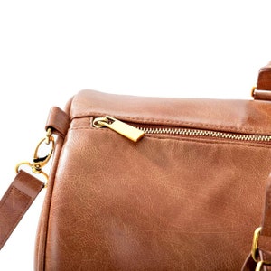 May include: A brown leather duffel bag with a gold zipper and a gold zipper pull. The bag has a strap with a gold clasp.