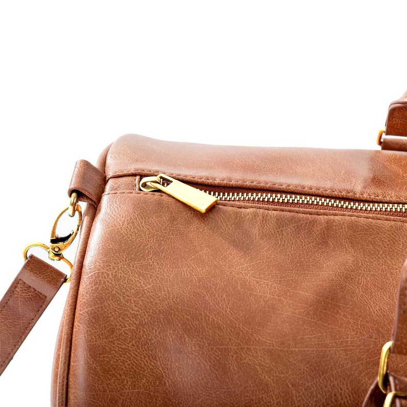 May include: A brown leather duffel bag with a gold zipper and a gold zipper pull. The bag has a strap with a gold clasp.