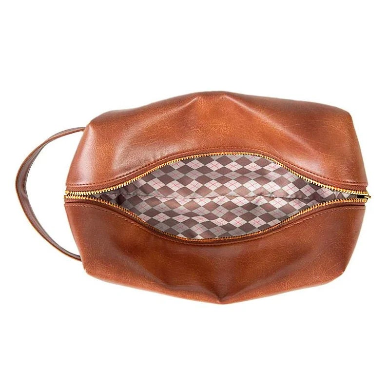 May include: A brown leather travel toiletry bag with a gold zipper and a checkered pink and gray lining.