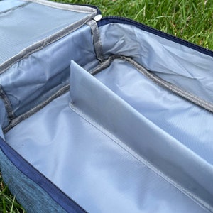 May include: A blue travel bag with a zipped opening and a grey interior. The bag has a divider inside to separate items.