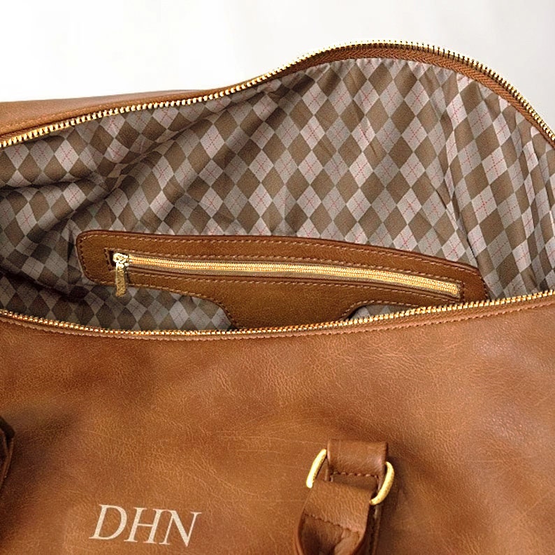 May include: A brown leather duffel bag with gold hardware and a zippered pocket inside. The bag has the initials "DHN" monogrammed on the front.