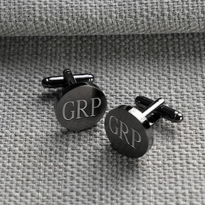 May include: A pair of round, dark gunmetal cufflinks featuring the engraved letters GRP in a serif font. Each cufflink has a polished, reflective surface and a standard T-bar swivel mechanism attached to the back for securing through shirt cuffs.