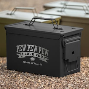May include: A black metal ammo box with a hinged lid and a carrying handle. The box features the text "PEW PEW PEW I LOVE YOU" in silver lettering, along with the names "Chase & Valerie". Other similar boxes are in the background.
