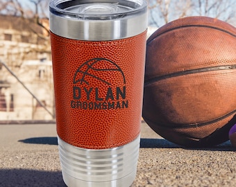 May include: A stainless steel tumbler with a brown leather basketball-textured wrap. The tumbler has a black engraved basketball and the text "DYLAN GROOMSMAN".