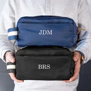 May include: Two toiletry bags, one navy blue with the initials "JDM" and one black with the initials "BRS".