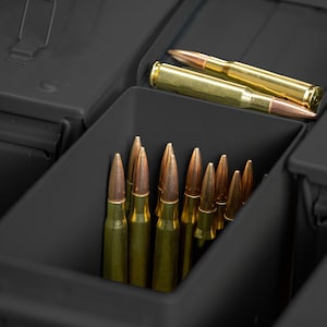 Peut inclure: Gros plan sur une bo&icirc;te &agrave; munitions gris fonc&eacute; avec plusieurs compartiments. Les compartiments contiennent divers types de munitions, notamment des balles en laiton avec des pointes cuivr&eacute;es. Les balles sont rang&eacute;es avec soin dans la bo&icirc;te.