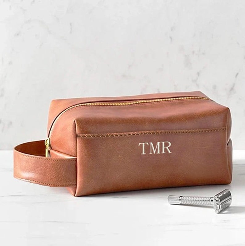May include: A brown leather travel bag with a gold zipper and a handle. The bag has the initials "TMR" embossed on the front.