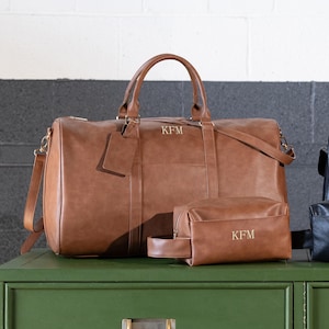 May include: A brown leather travel duffel bag with a matching brown leather toiletry bag. Both bags have the initials "KFM" embossed on them.