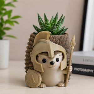 Può includere: Un vaso a forma di riccio color marrone chiaro con una texture dorsale spinosa, che indossa un elmo in stile spartano con cresta. Il riccio tiene in mano uno scudo rotondo con un simbolo lambda greco e una lunga lancia, contenente una succulenta.