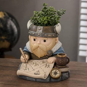 May include: A decorative planter shaped like a Viking character wearing a horned helmet, holding a pen over a map. The figure features a beard, a blue cloak, a small mug, a book, and a compass. A green plant sits in the top of the helmet.