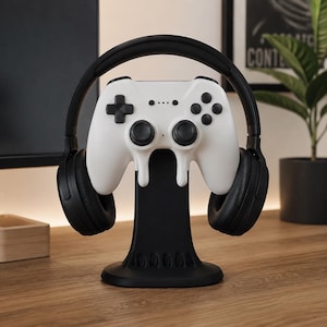 May include: A black gaming controller and headset stand featuring a white video game controller with a melting drip design mounted on the front, with black over-ear headphones resting on the side arms of the stand for organized storage.