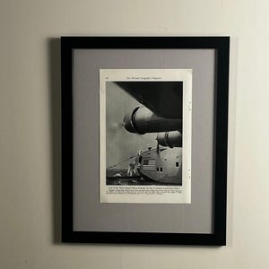 May include: A framed black and white vintage print from The National Geographic Magazine featuring a seaplane titled Dixie Clipper. The image shows the aircraft on water with a small boat nearby and an American flag on the fuselage side.